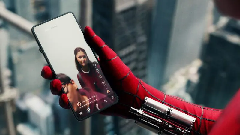 Spider-Man's gloved hand holding a phone playing a video of Ned and MJ