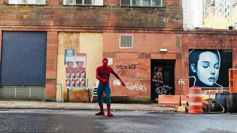 Spider-Man standing on a Queens street in front of a mural